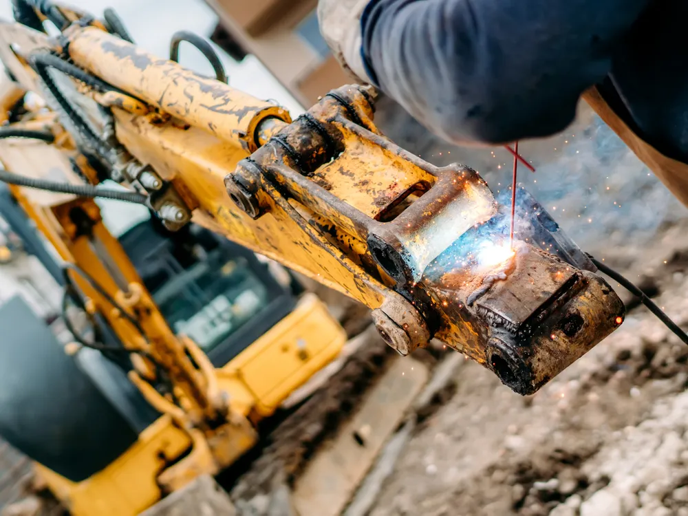 Welding repair in progress on an excavator arm